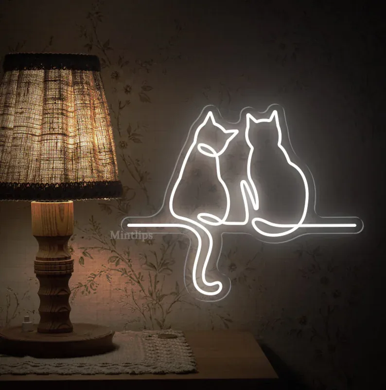 Two cats outline neon sign in warm white beside a table lamp