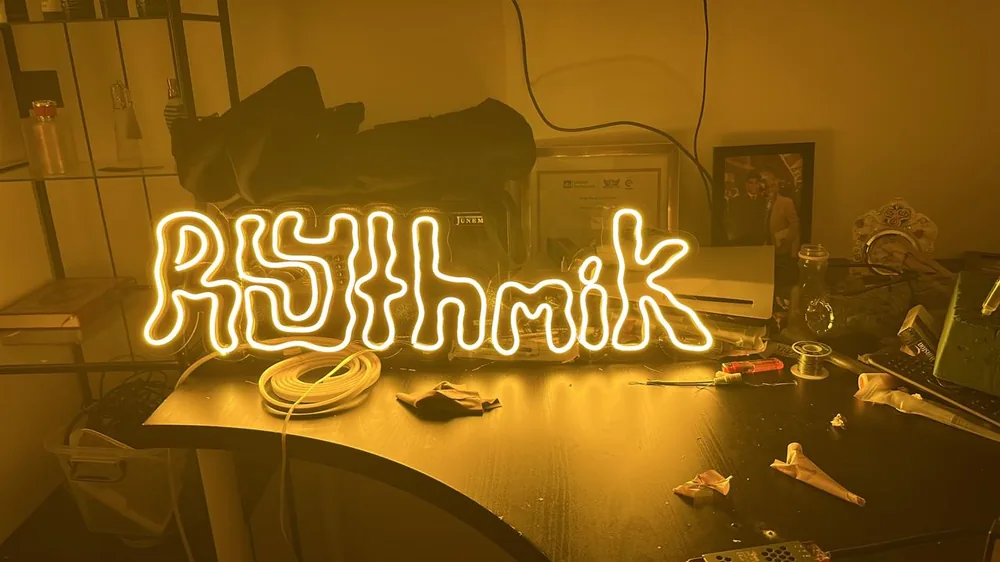 Rhythmik logo neon in warm yellow on a workbench